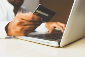 Nahaufnahme eines Laptops und den Händen einer Person, welche eine Bankkarte in der Hand hält.